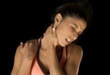 una mujer atlética joven se agarra el cuello y los hombros y hace un gesto de dolor