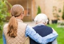 una cuidadora pone su brazo alrededor de una mujer de edad avanzada mientras caminan afuera
