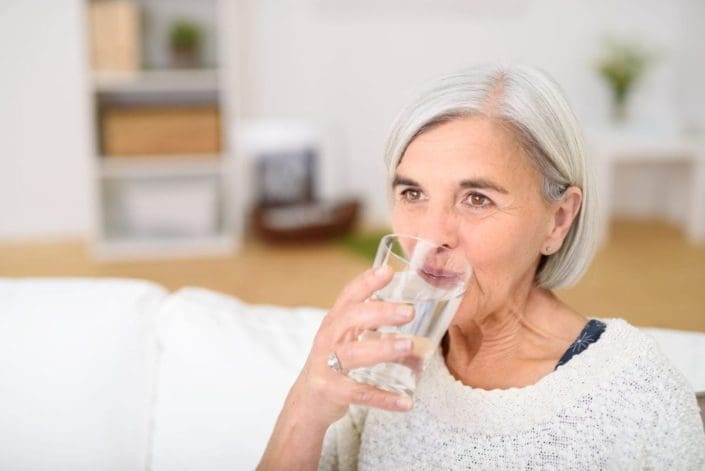 mujer de mediana edad bebe un vaso de agua en la sala de estar y mira a la distancia