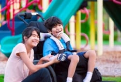 Niño pequeño con parálisis cerebral sentado en su silla de ruedas que se ríe junto a su hermana