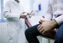 hombre sentado en una mesa de examen que está siendo asesorado en el consultorio de un médico