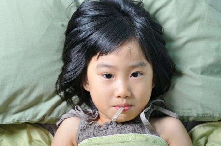 una niña pequeña en la cama con un termómetro en la boca