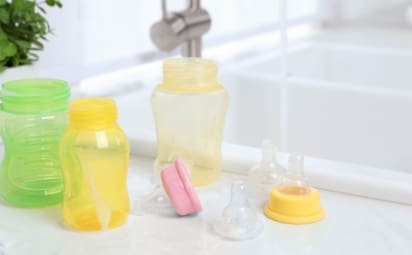 Baby bottles and nipples sit on a white countertop beside the kitchen sink after being washed.