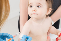 A gloved doctor is poised to give a toddler a shot in the arm.