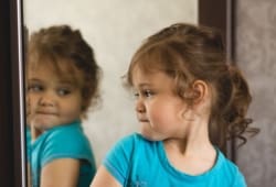 Young girl looking at her reflection in the mirror