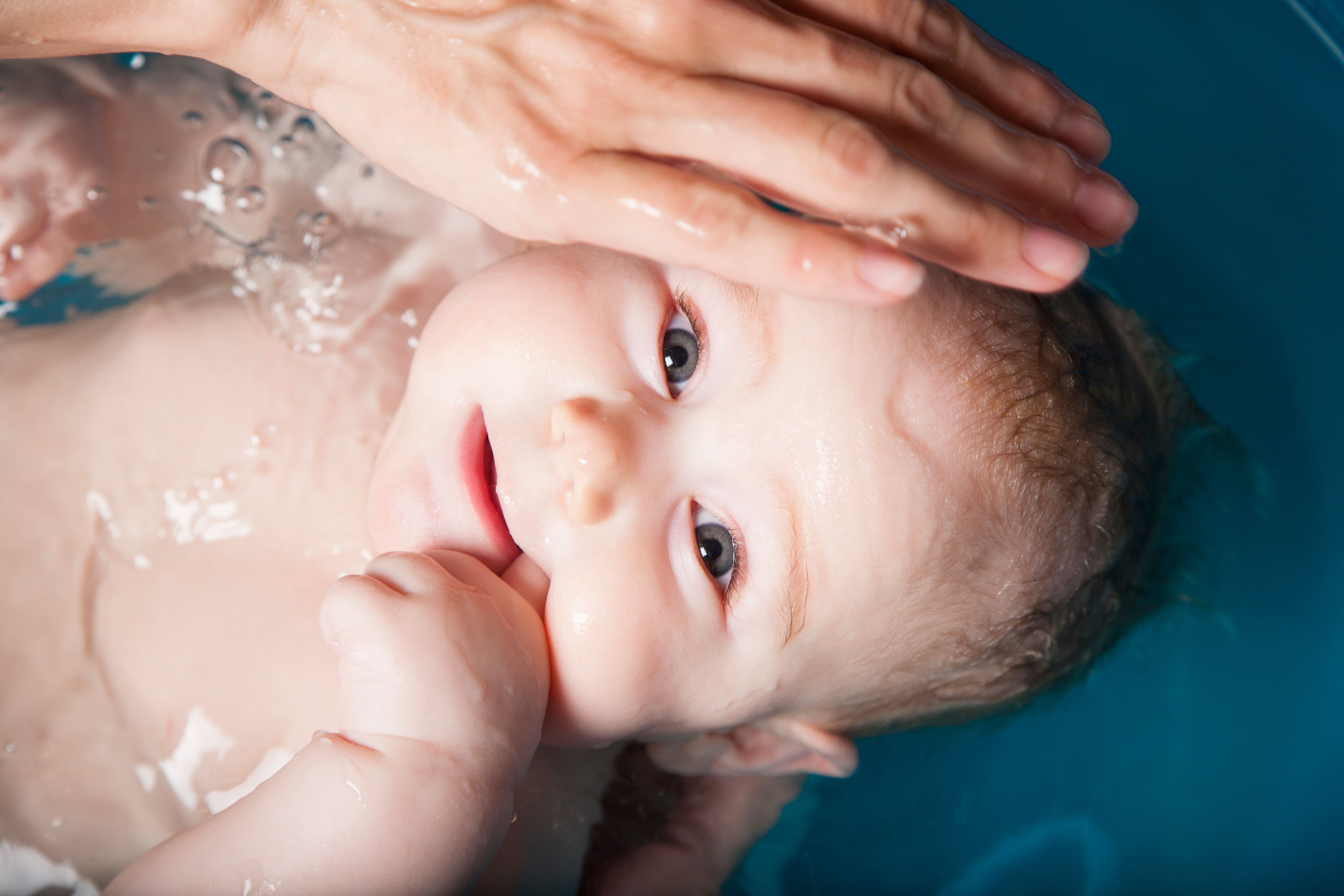 Bebé siendo bañado por su madre en una bañera de plástico azul.