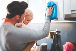 Un padre joven limpia la cocina mientras sostiene a su hija.