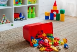 Algunos bloques de colores se derraman de un contenedor rojo en el piso de la sala de juegos de un niño.