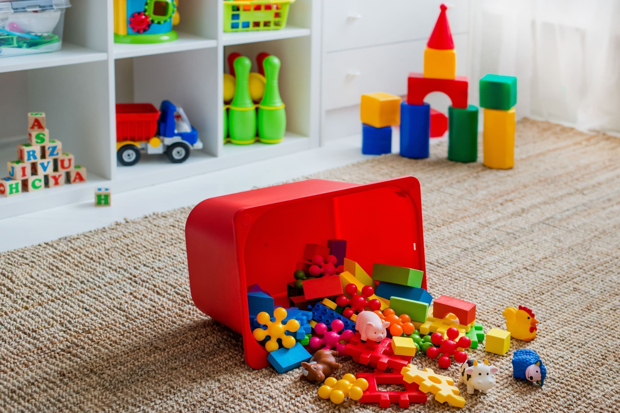 Algunos bloques de colores se derraman de un contenedor rojo en el piso de la sala de juegos de un niño.